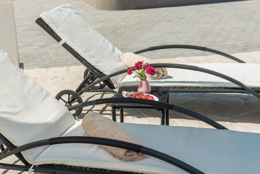 Eine Liege mit weißem Kissen, ein kleiner Tisch mit Blumen in einer Vase und eine Schale mit Obst.