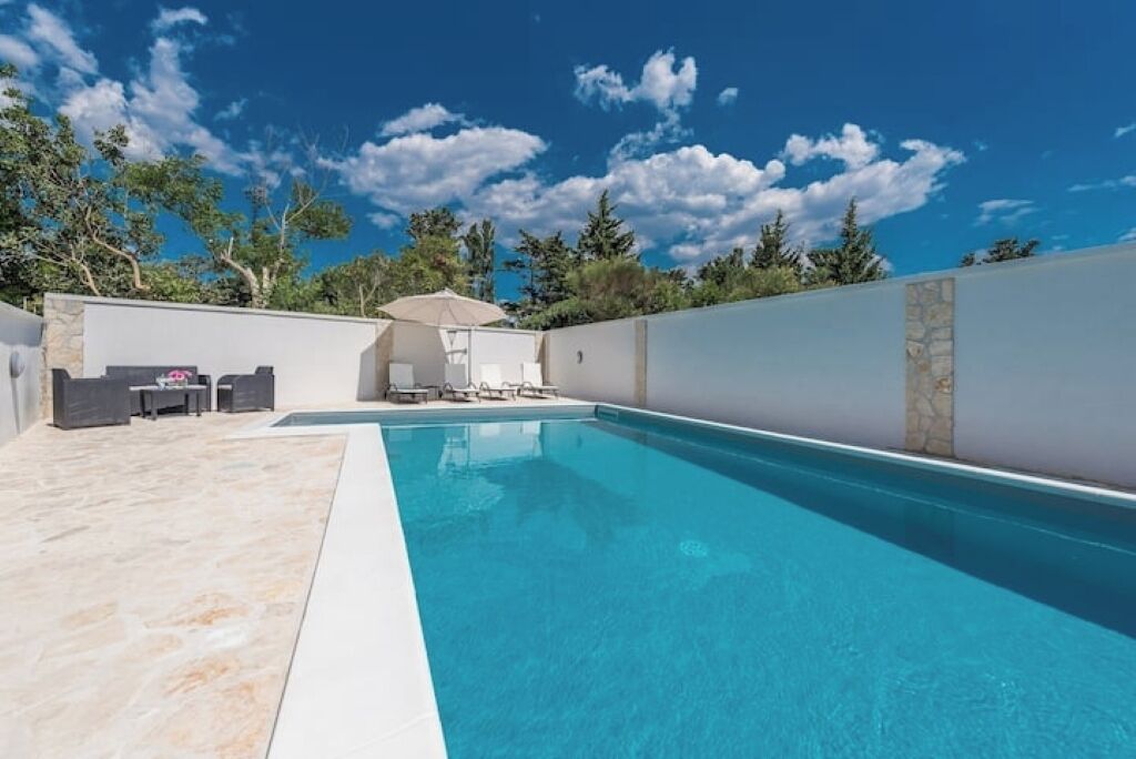 Una piscina con terraza de piedra, sillas de descanso y una mesa.