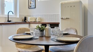 Un coin repas avec une table ronde dressée pour quatre personnes, un réfrigérateur blanc et une fenêtre donnant sur des immeubles.