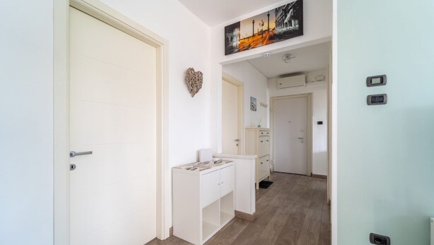 Un couloir avec une porte blanche, un bureau blanc doté de tiroirs, une décoration en forme de cœur et un tableau accroché au-dessus du bureau.