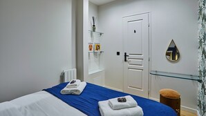 Ett hotellrum med en säng, en glashylla med toalettartiklar, en vit dörr och en spegel på väggen.