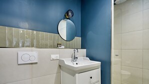 Un baño con lavamanos blanco, espejo y zona de ducha.