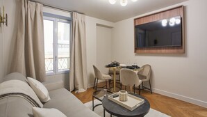 A modern living room with a sofa, a dining table with chairs, a small round table with a tray, and a large mirror on the wall. - New apartment Center of Paris/Le Marais (Paris)