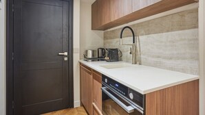 A compact kitchen with a dark door, wooden cabinets, a white countertop, a stainless steel sink, and a built-in oven. - New apartment Center of Paris/Le Marais (Paris)