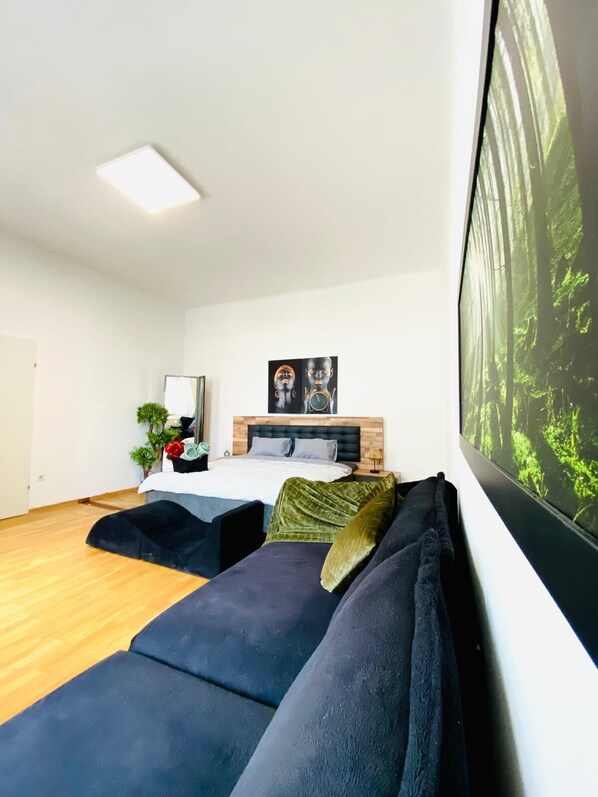 A modern bedroom with a bed, two sofas, a nightstand, a mirror, and a large window with a forest view. - Bright 2BR Apartment Near Westbahnhof (Vienna)