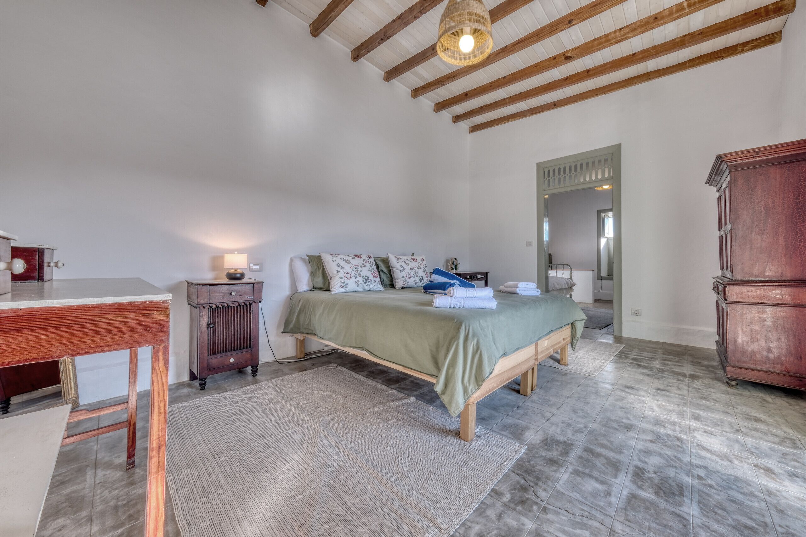 A bedroom with a bed, wooden furniture, a desk, and a hanging light fixture.