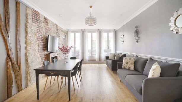 A spacious living area with a dining table, grey sofa, and a chandelier.