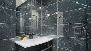 A bathroom with black marble tiles, a white sink, gold fixtures, and a large mirror.