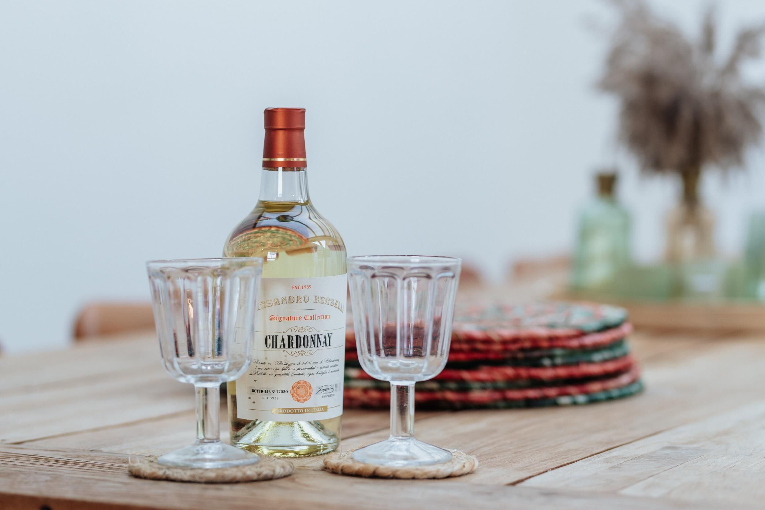 A bottle of chardonnay and two glasses on a wooden table.