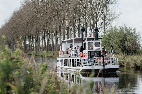 A riverboat with passengers, surrounded by trees and calm water.