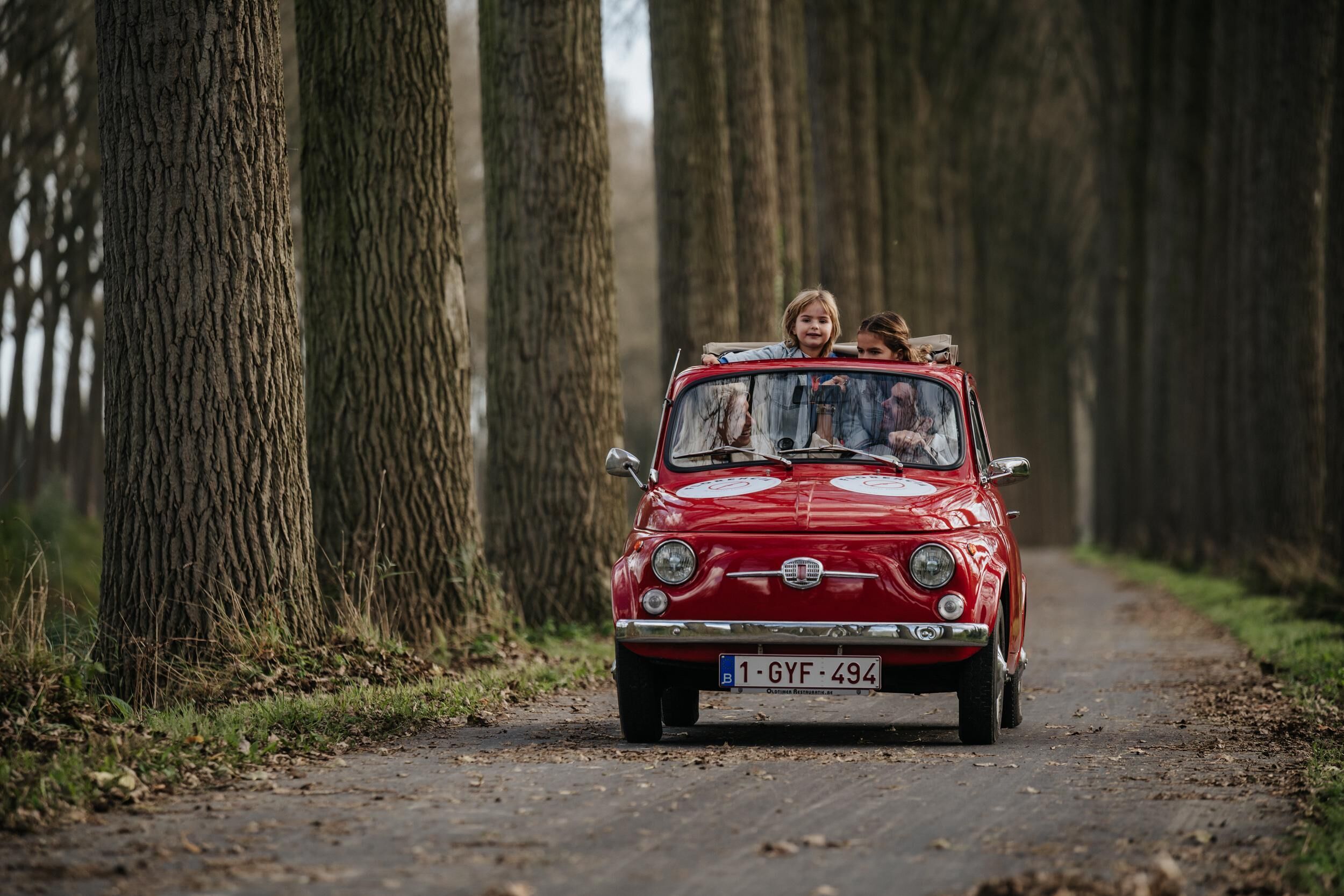 Un coche rojo antiguo con una placa de matrícula en un camino forestal.