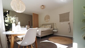 A modern bedroom with a bed, bedside tables, a bedside lamp, a wall-mounted artwork, and a large window allowing natural light. - Beautifully styled studio apartment (Betgummole)