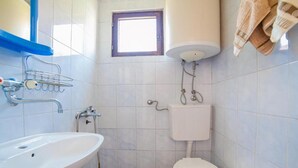 Une petite salle de bain avec un lavabo blanc, des toilettes et une fenêtre située au-dessus des toilettes.