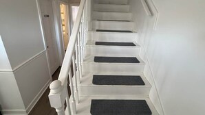A white staircase with black risers and a handrail, leading to a door at the top.