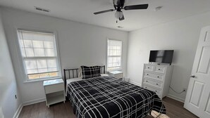 A bedroom with a bed, two windows, a ceiling fan, a dresser, and a TV.