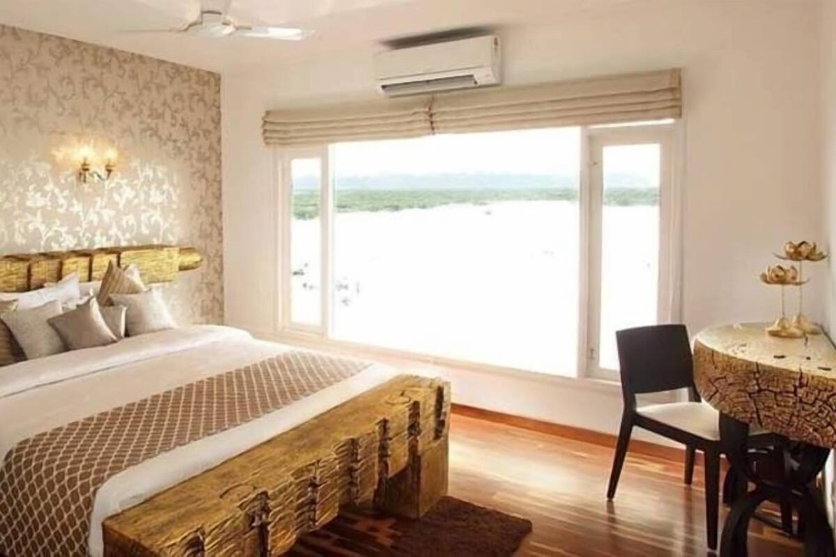 A bedroom with a bed, a wooden bench, a chair, a table, and a view of the outdoors.