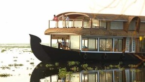 A houseboat with a balcony and large windows, floating on water. - The Boat Company (Cherthala)
