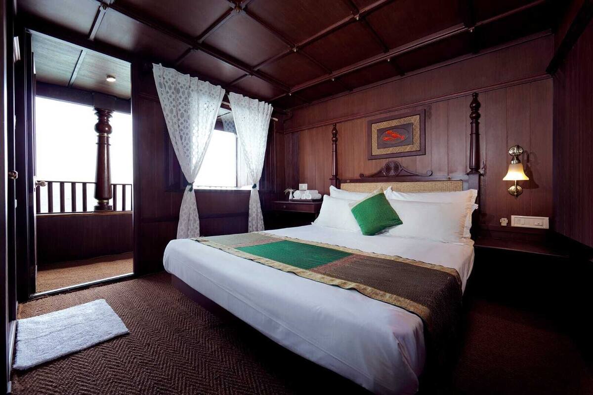 A hotel room with a large bed, a wooden headboard, a nightstand, a lamp, and a window with curtains.