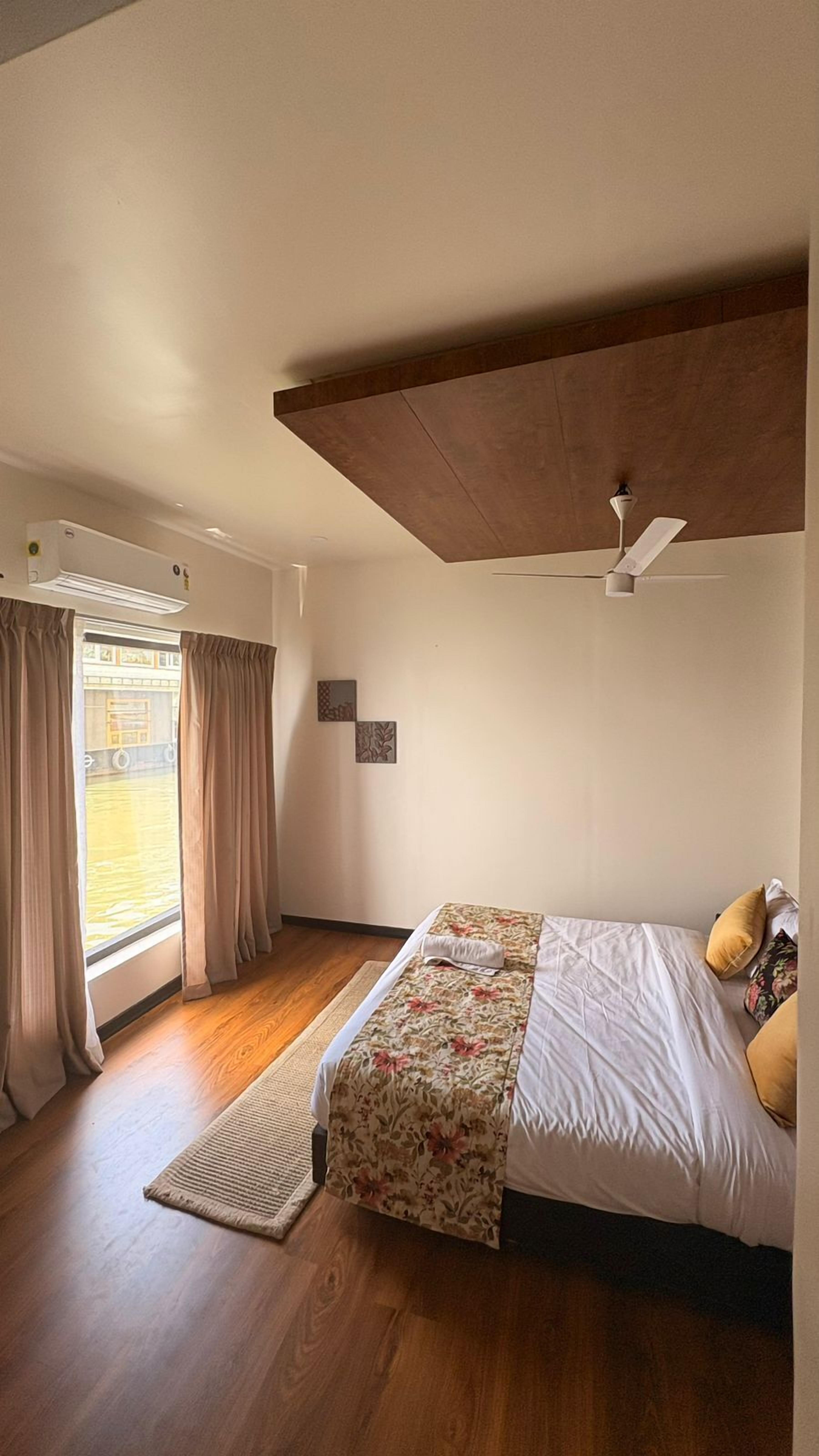 A bedroom with a bed, wooden flooring, a ceiling fan, and a window with curtains.