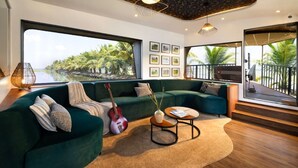 A modern living room with a green sofa, a guitar, and a view of palm trees and water. - The Boat Company (Cherthala)