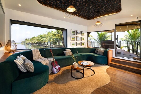 A modern living room with a green sofa, a guitar, and a view of palm trees and water.
