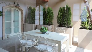 A white dining table with four chairs, surrounded by potted plants and a white cabinet. - 5 Appartamenti di lusso sul Lago di Garda (Affi)