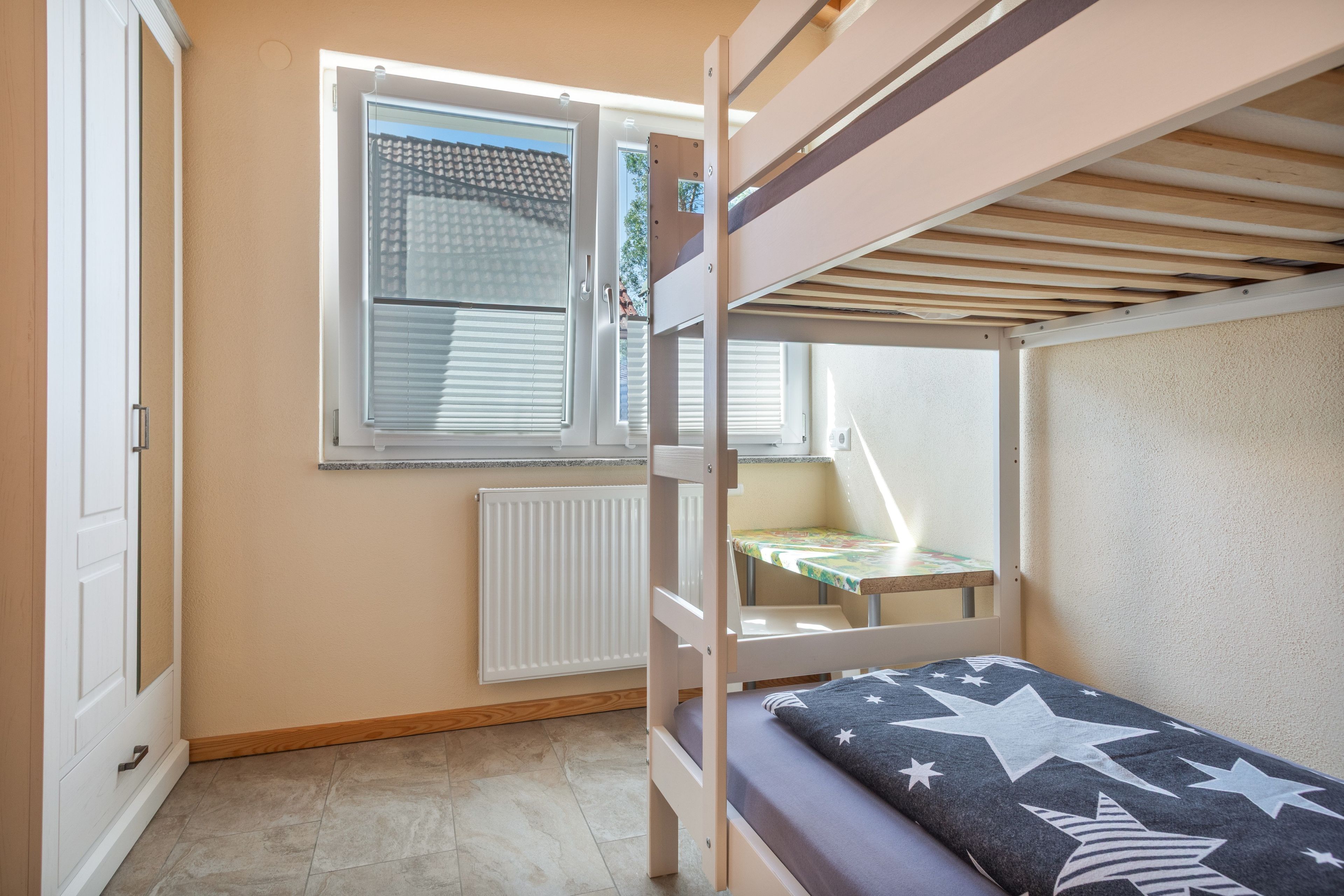 Ein Schlafzimmer mit Etagenbetten, einem Fenster, einer Heizung und einem kleinen Tisch.