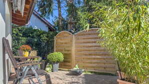 Eine Terrasse mit Holzzaun, einem Tisch mit Stühlen und Kübelpflanzen.