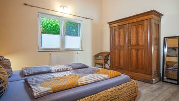 Een slaapkamer met een bed, een kledingkast, een raam met jaloezieën en een stoel.