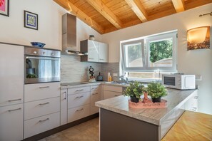 A modern kitchen with white cabinets, stainless steel appliances, and a window with a view of greenery.