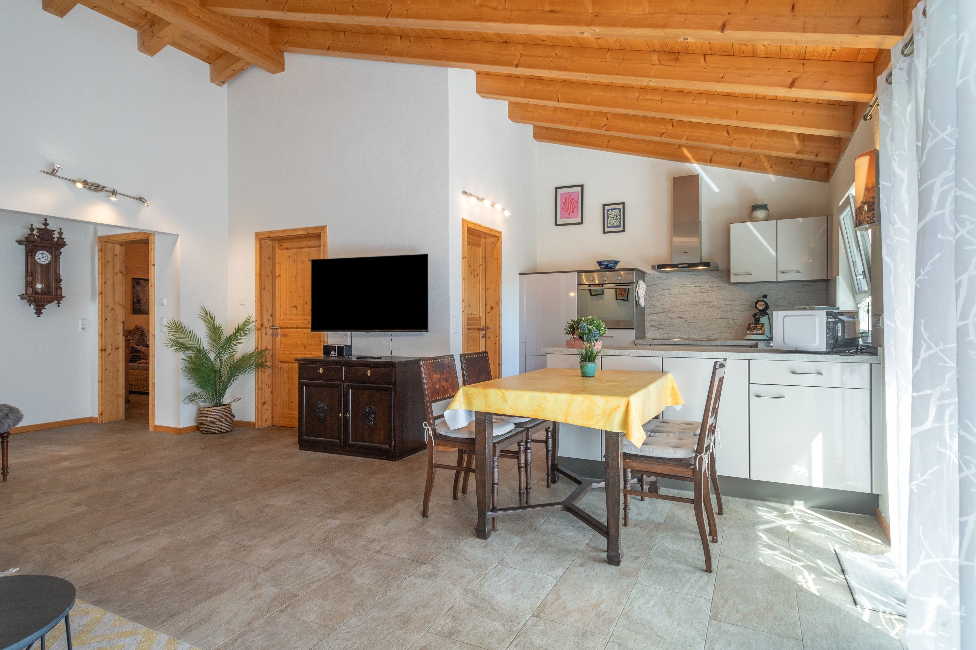 Un vaste espace de vie doté d’un plafond en bois, d’une table à manger avec des chaises, d’un téléviseur à écran plat et d’un coin cuisine avec des placards et des appareils électroménagers.