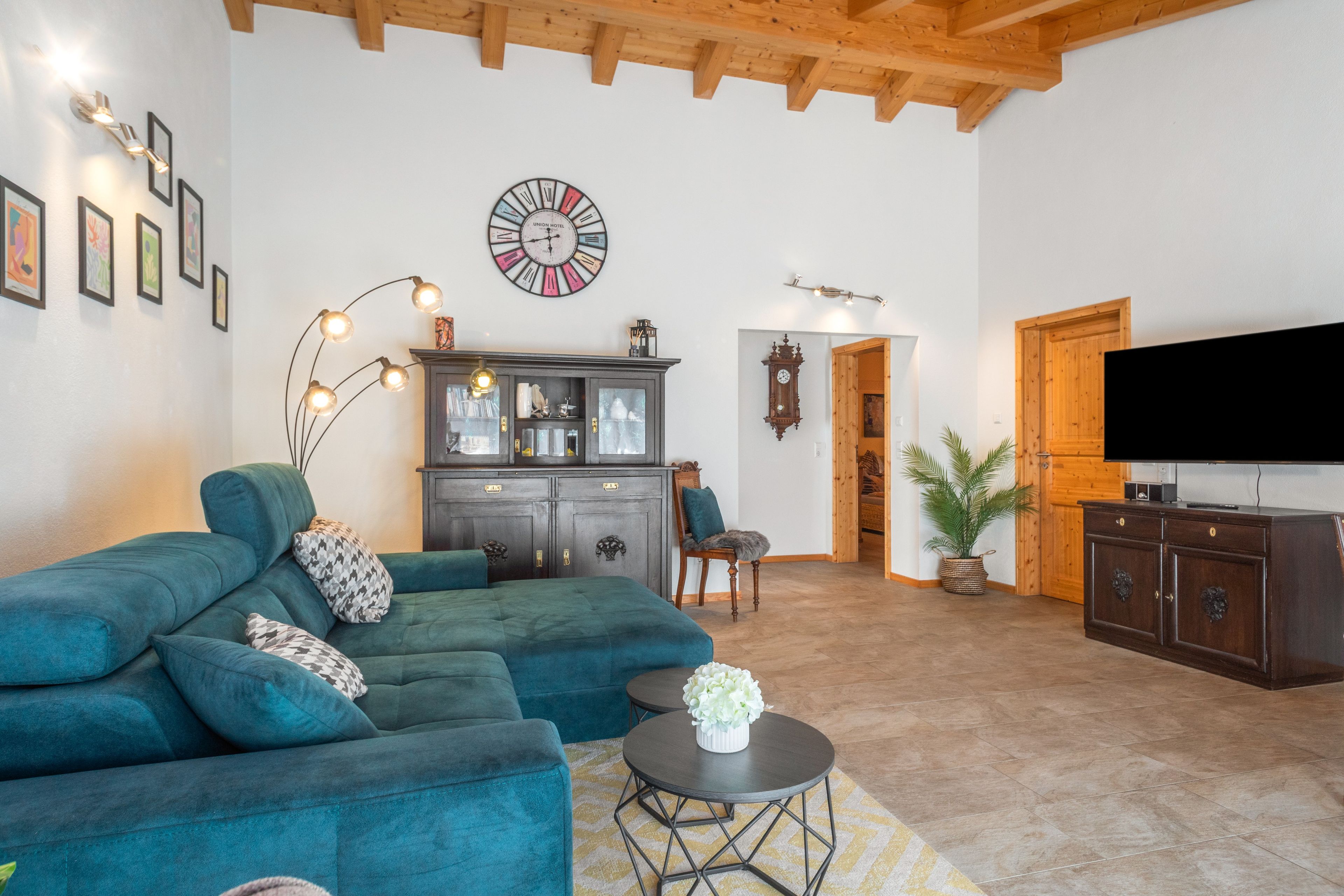 A living room with a sectional sofa, a cabinet, a clock, and a television.