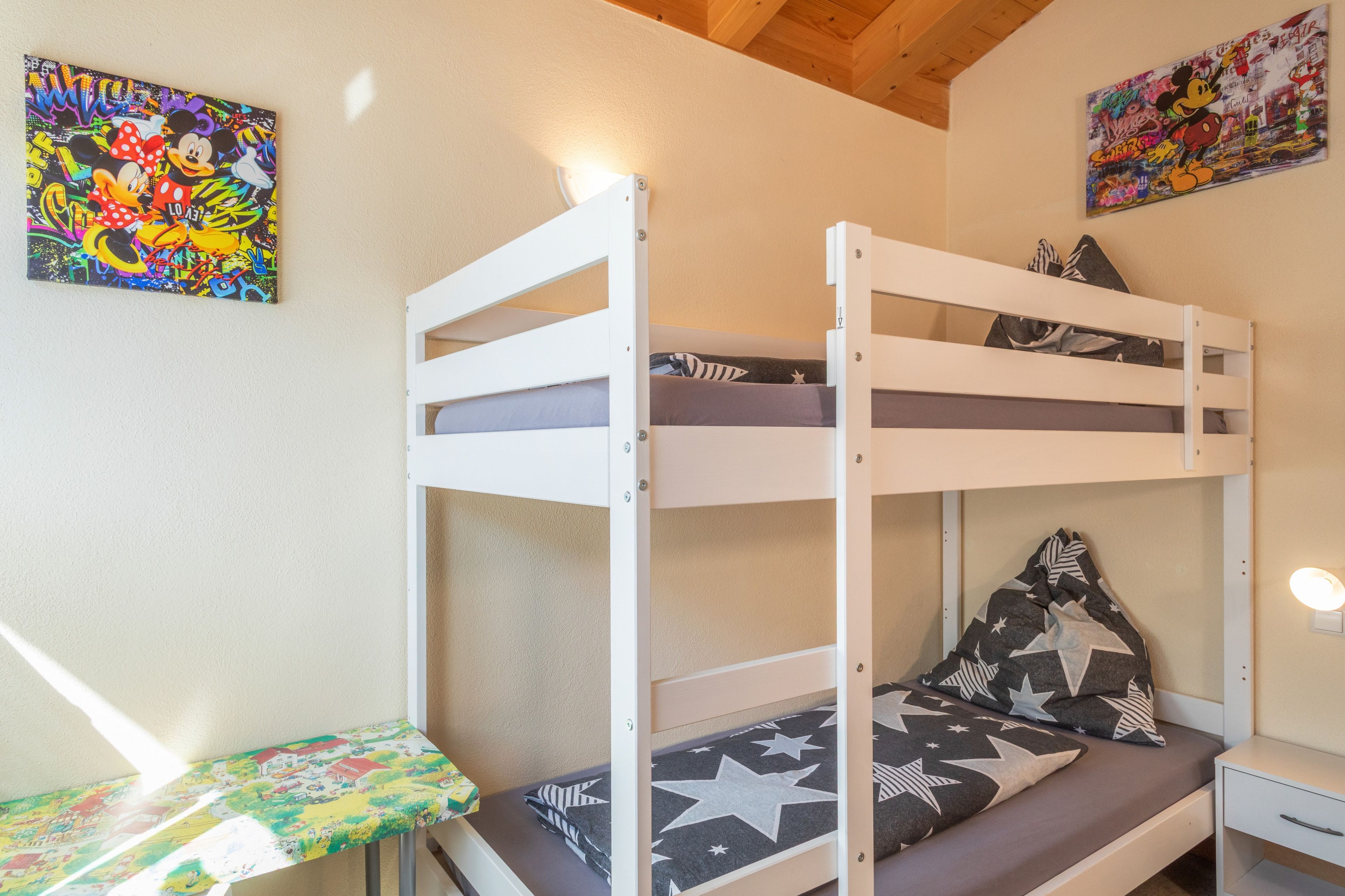 Ein Etagenbett mit einem Kissen mit Sternenmuster und einem kleinen Tisch mit bunten Tischdecken.