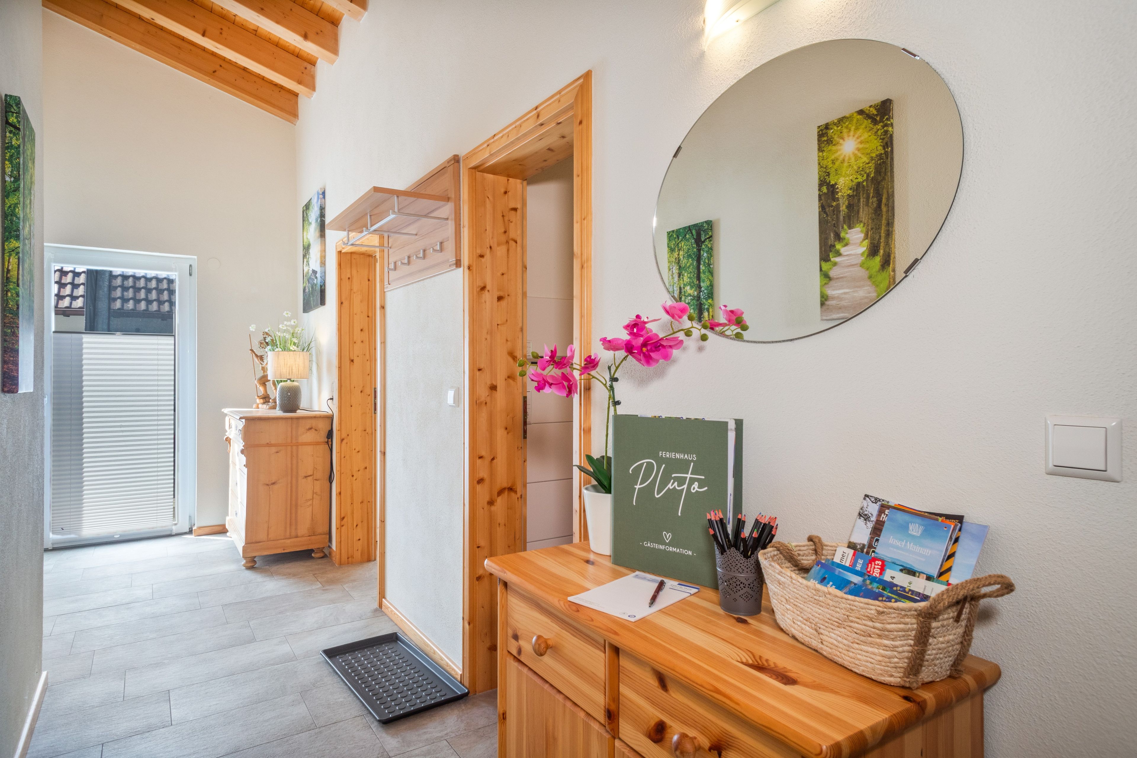 Un comptoir d’accueil en bois, agrémenté d’un miroir, d’un vase avec des fleurs roses et d’un tableau encadré au mur.