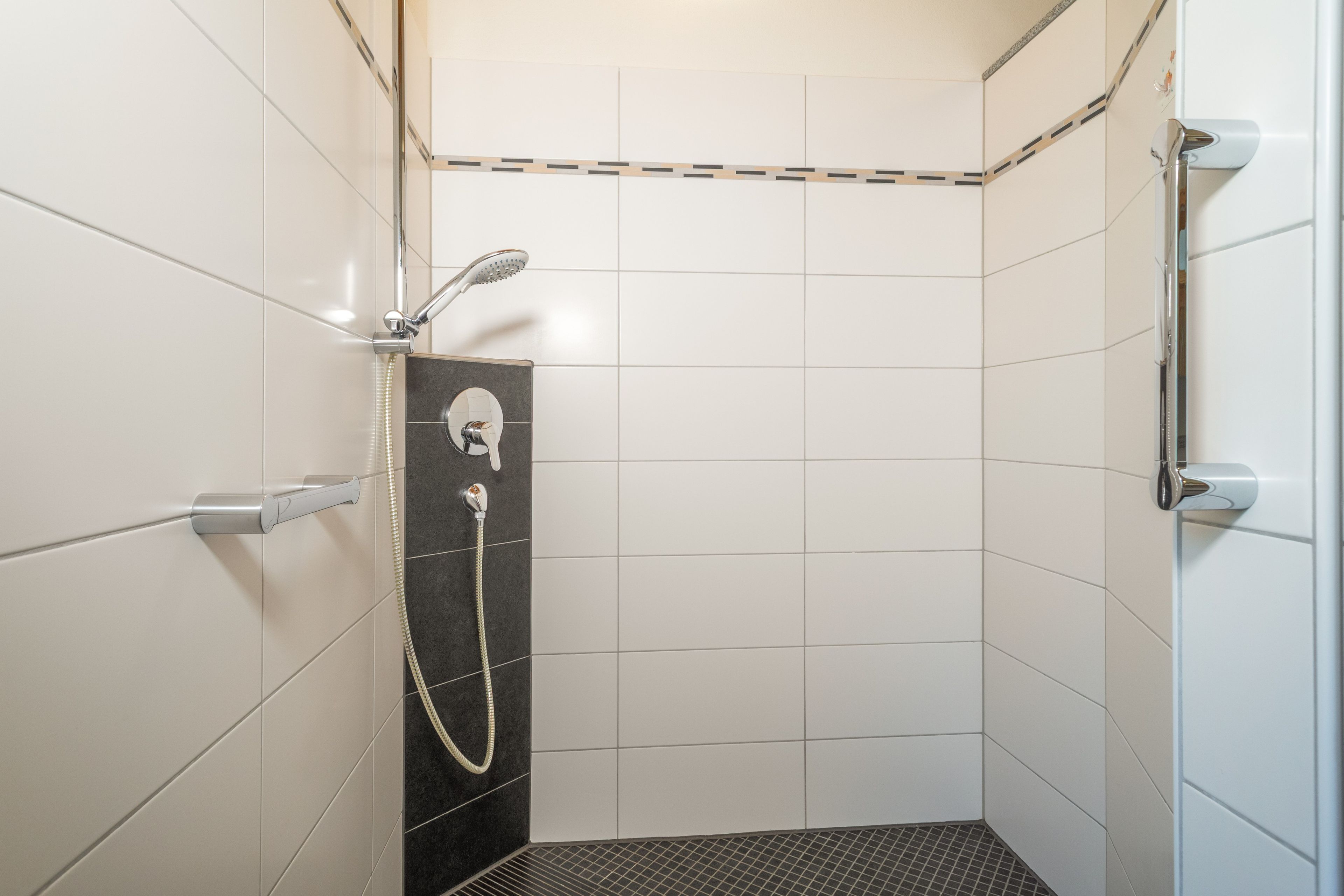 Ein kleines Duschbad mit gefliesten Wänden, einer Handbrause und einem am Wand montierten Wasserhahn.