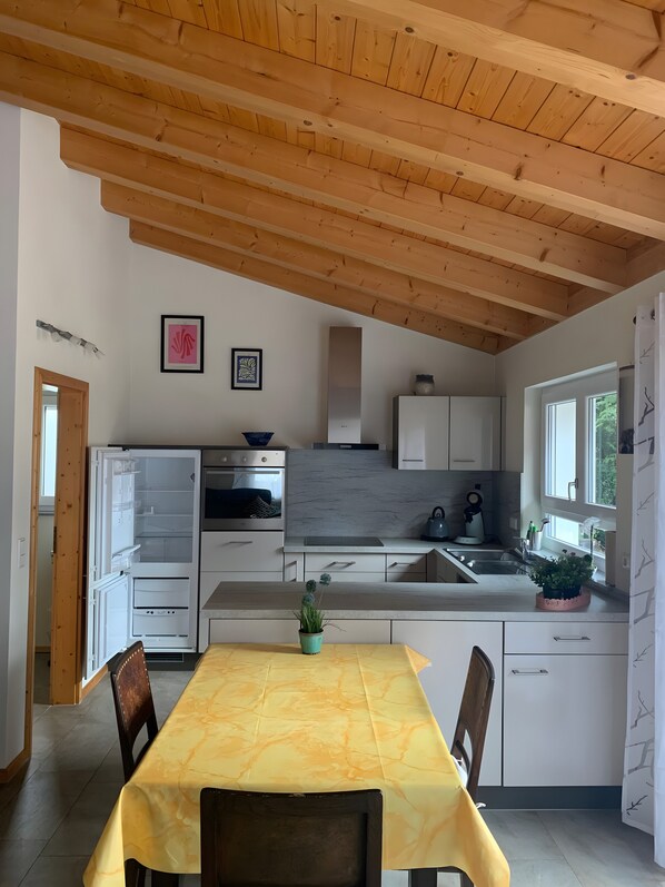 A modern kitchen with wooden beams, white cabinets, a marble countertop, and a dining table with chairs.