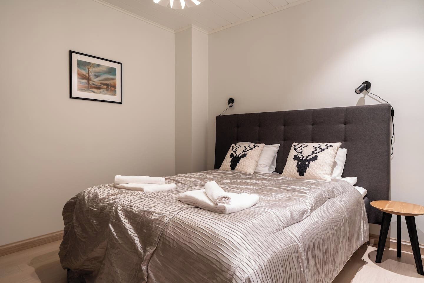 Ein ordentlich bezogenes Bett mit grauem Kopfteil, weißen Kissen und einem gerahmten Bild an der Wand.