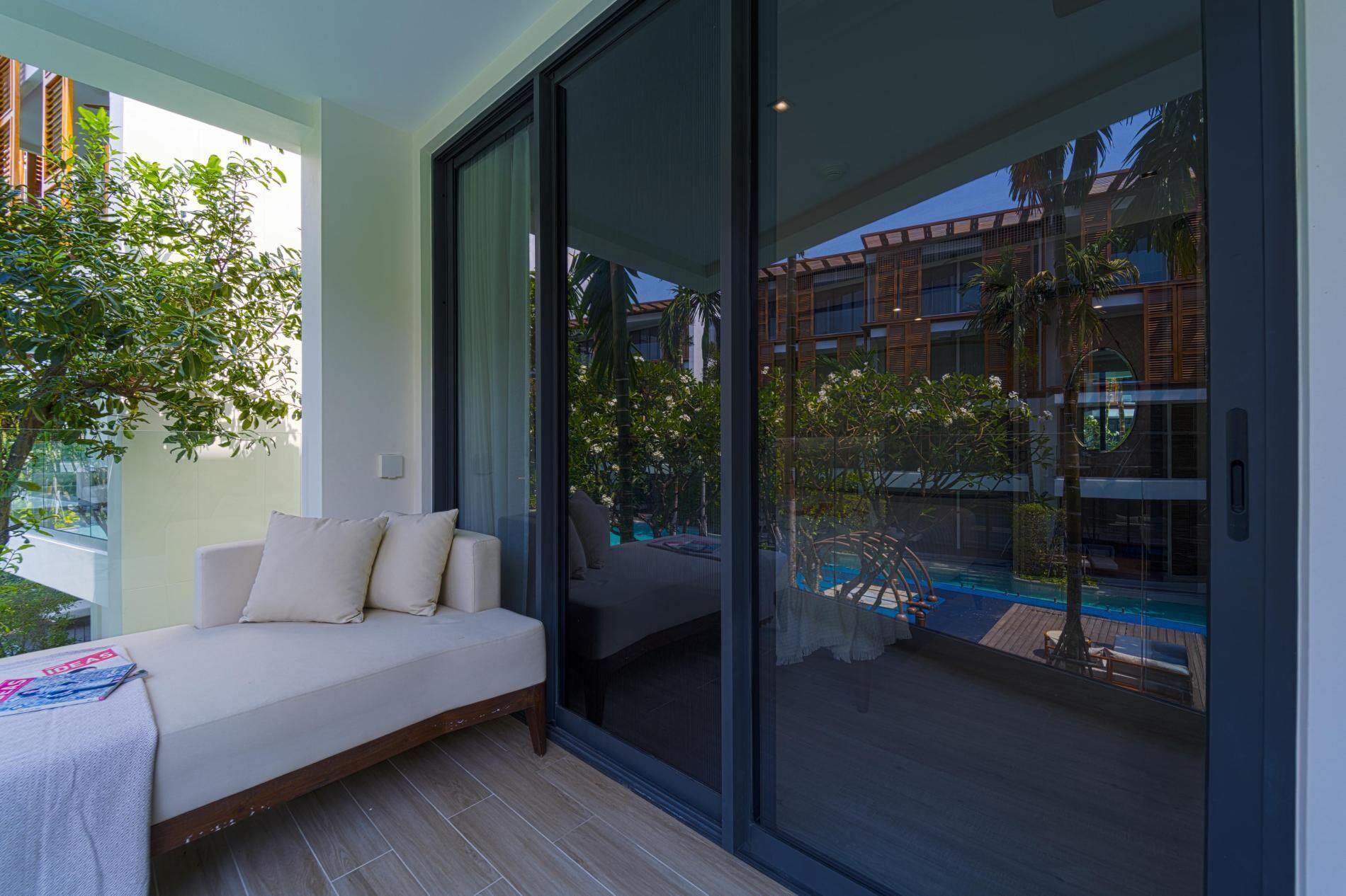 A modern room with a sofa, a large sliding glass door, and a view of a pool and buildings.