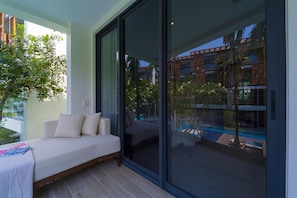 A modern room with a sofa, a large sliding glass door, and a view of a pool and buildings. - InterContinental Residences 2Bedroom IRA (Hua Hin)