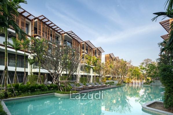 A modern hotel with a pool area, featuring multiple floors with balconies, surrounded by lush greenery. - InterContinental Residences 2Bedroom IRA (Hua Hin)