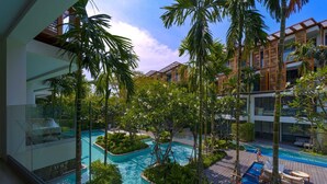 A modern hotel with a large outdoor swimming pool surrounded by lush greenery and palm trees. - InterContinental Residences 2Bedroom IRA (Hua Hin)