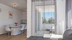 Un soggiorno moderno con un divano grigio, una zona pranzo con sedie bianche e una cucina sullo sfondo.