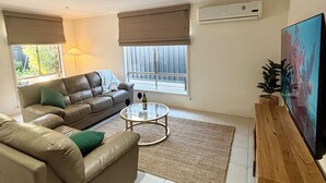 Ett modernt vardagsrum med en soffa i läder, ett soffbord i glas och en platt-TV som står på ett träställ.