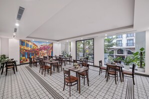 A spacious dining area with multiple tables and chairs, a large mural on the wall, and large windows offering a view of the outside. - Zen Lotus Hotel & Apartment (Da Nang)