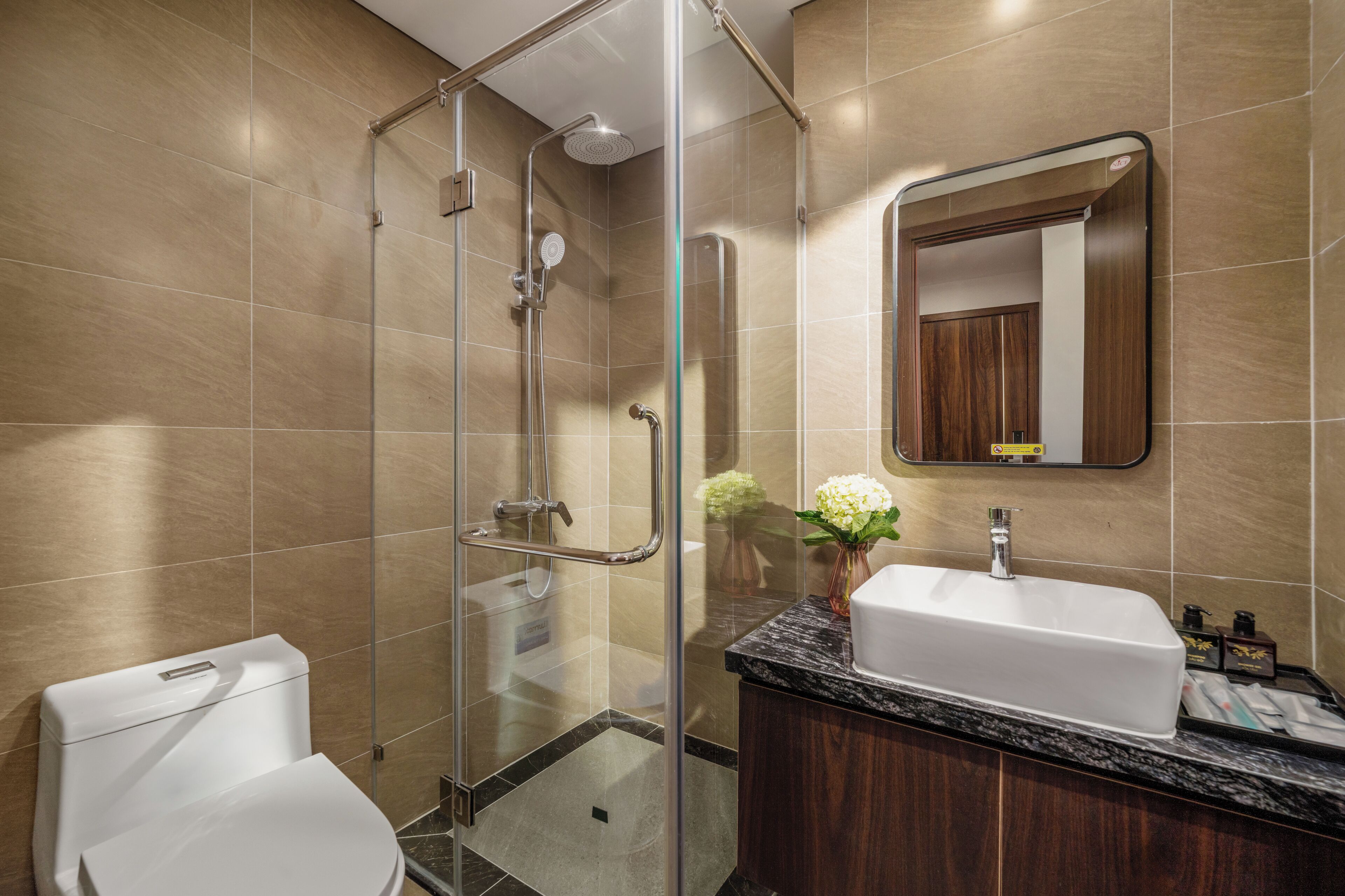 A modern bathroom with a glass-enclosed shower, a white toilet, a wooden vanity with a sink, and a mirror above the mirror cabinet.