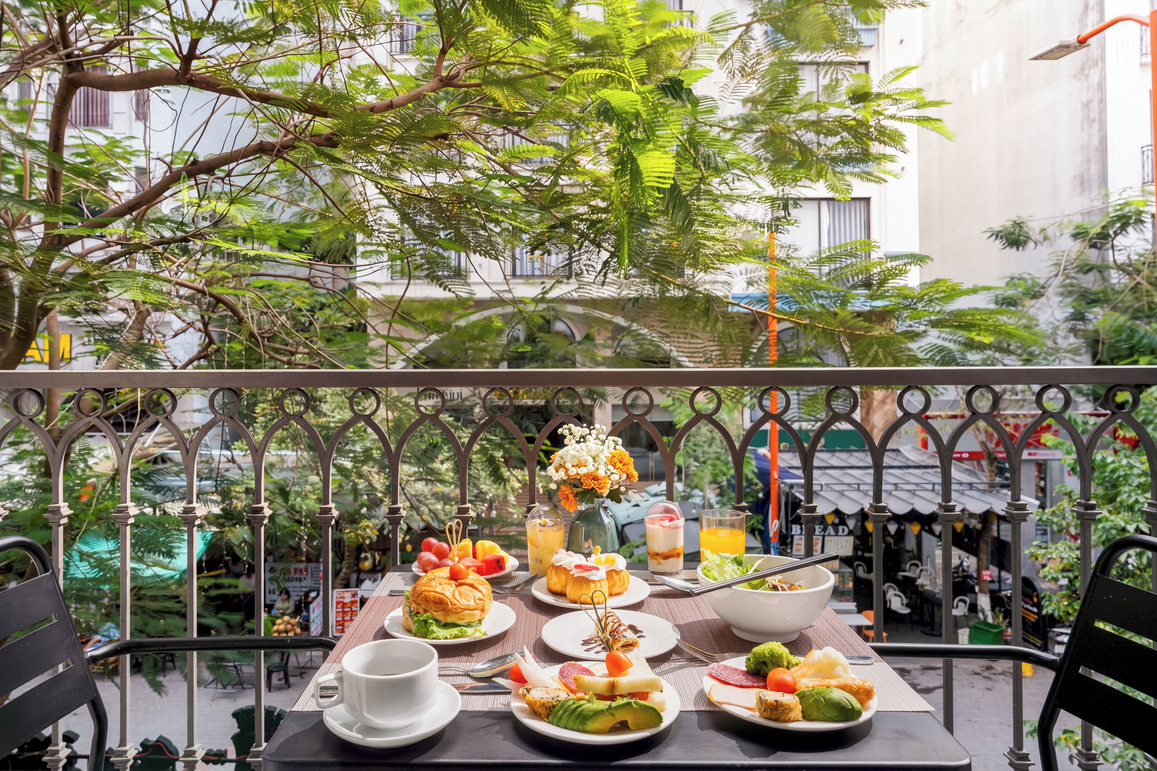 An outdoor dining area with a table set for lunch, surrounded by greenery and a view of the city.