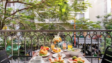 An outdoor dining area with a table set for lunch, surrounded by greenery and a view of the city.