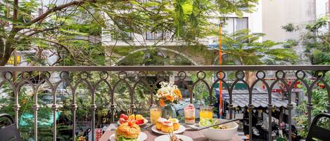 An outdoor dining area with a table set for lunch, surrounded by greenery and a view of the city.