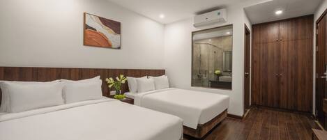 A hotel room with two beds, a ceiling fan, an air conditioning unit, a bathroom with a mirror, and wooden flooring.