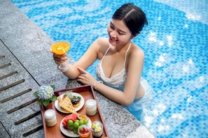 A person sitting by a pool with a tray of food and a drink. - Zen Lotus Hotel & Apartment (Da Nang)